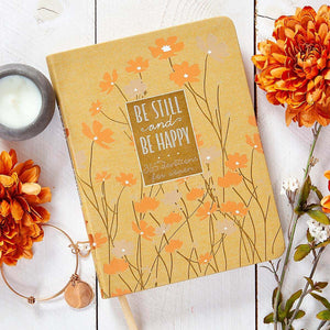 Notebook with floral design and motivational quote on a wooden surface with flowers and a candle.