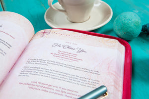 Open book with a pink zipper case on a teal surface with a cup and saucer.