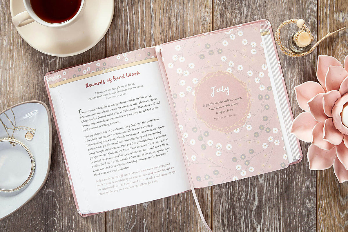 Pink planner with floral design on a wooden surface with a cup of tea and flower.