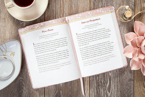 Open book with text on a wooden surface with a cup of tea and flower.