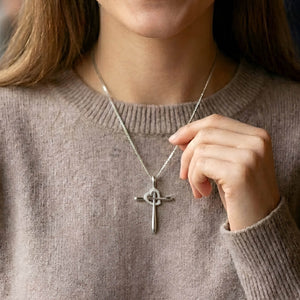 Person wearing a silver necklace with a cross pendant