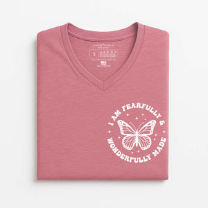 Folded pink t-shirt with a white butterfly Christian graphic on a light gray background