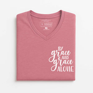 Folded pink t-shirt with 'By grace and grace alone' text on a white background