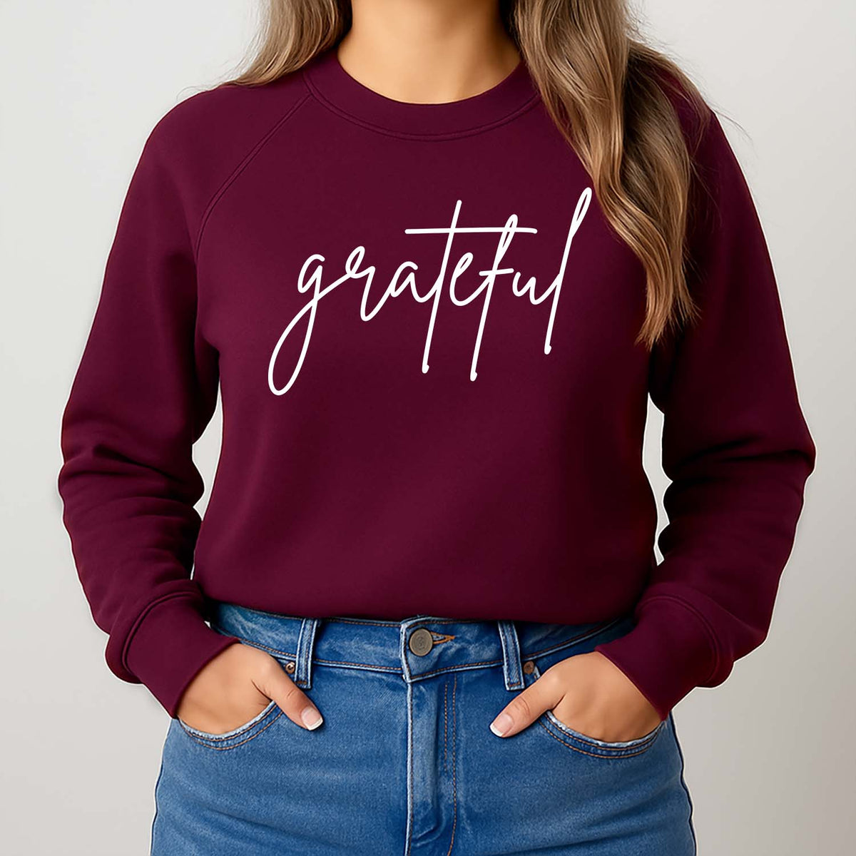 Maroon sweatshirt with 'grateful' text worn by a woman standing against a plain background