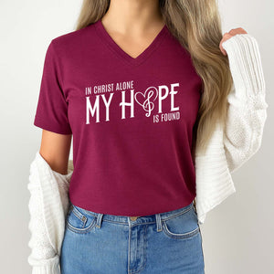 Person wearing a maroon t-shirt with a religious quote design on a plain background