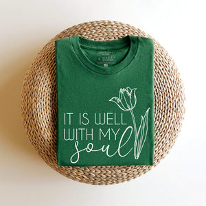 It is well with my soul shirt in green folded atop a woven basket