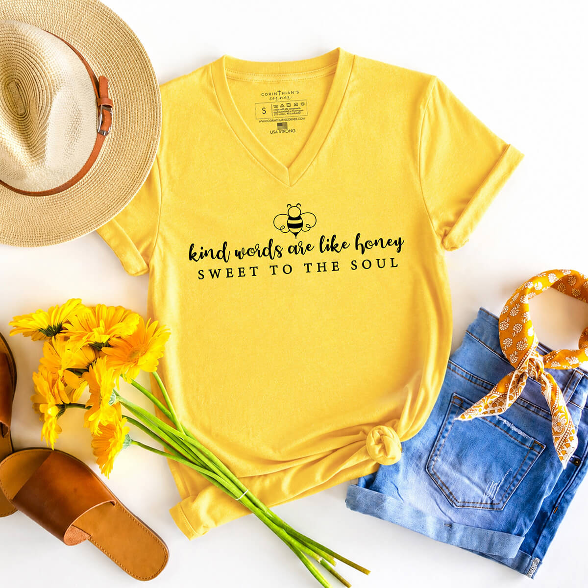 Yellow t-shirt that reads kind word are like honey sweet to the soul alongside a straw hat, flowers, and denim shorts