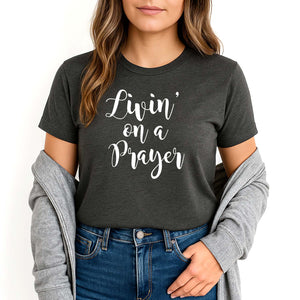 Woman wearing a dark gray t-shirt with 'Livin' on a Prayer' text, paired with a gray jacket and blue jeans.