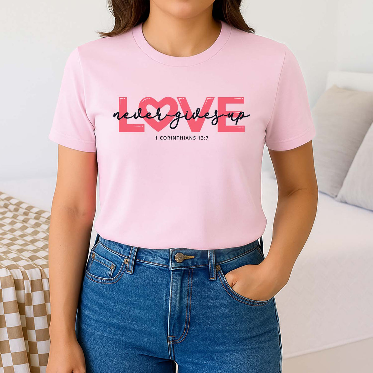 Woman wearing a pink t-shirt with 'LOVE never gives up' text, standing against a neutral background.