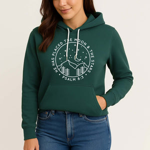 Woman wearing a green hoodie with a Bible verse design and nature design on a plain background