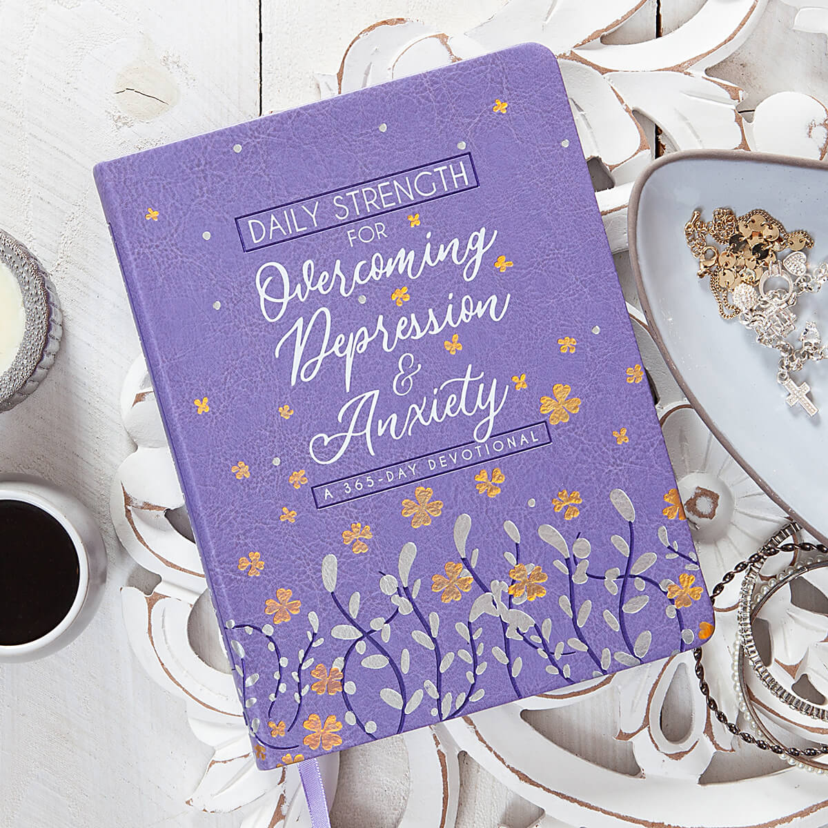 Purple book titled 'Daily Strength for Overcoming Depression & Anxiety' on a decorative surface with a cup of coffee.