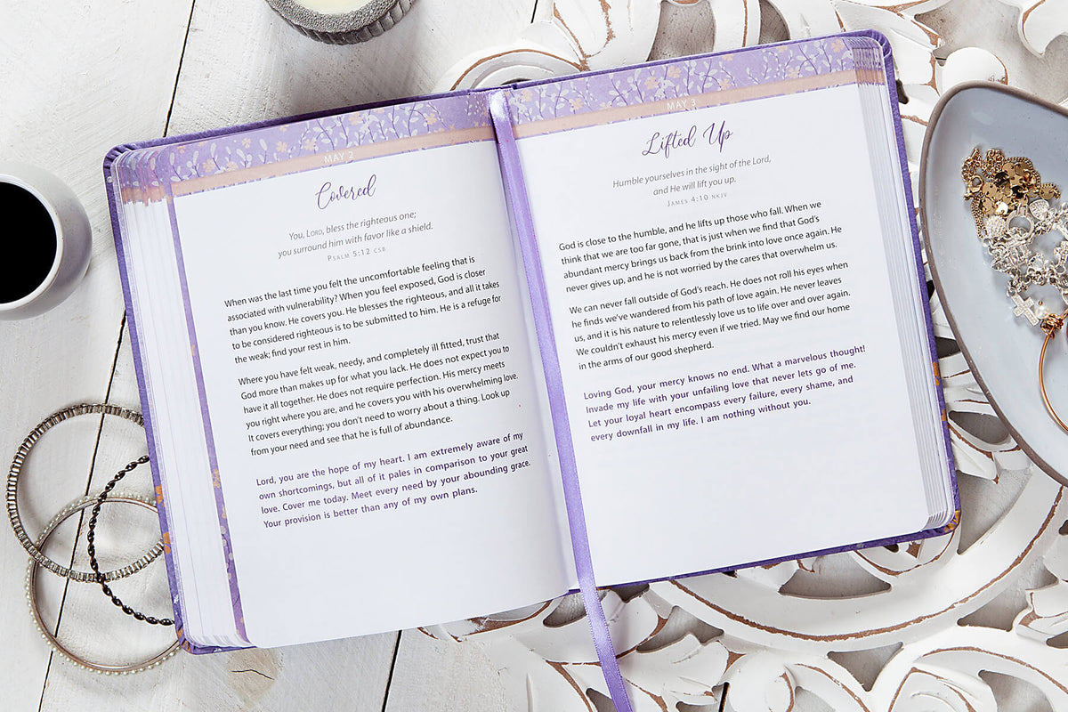 Open book with purple cover on a decorative surface with jewelry and a cup.