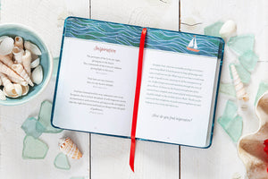 Open book with a red bookmark on a wooden surface surrounded by seashells and decorative items.