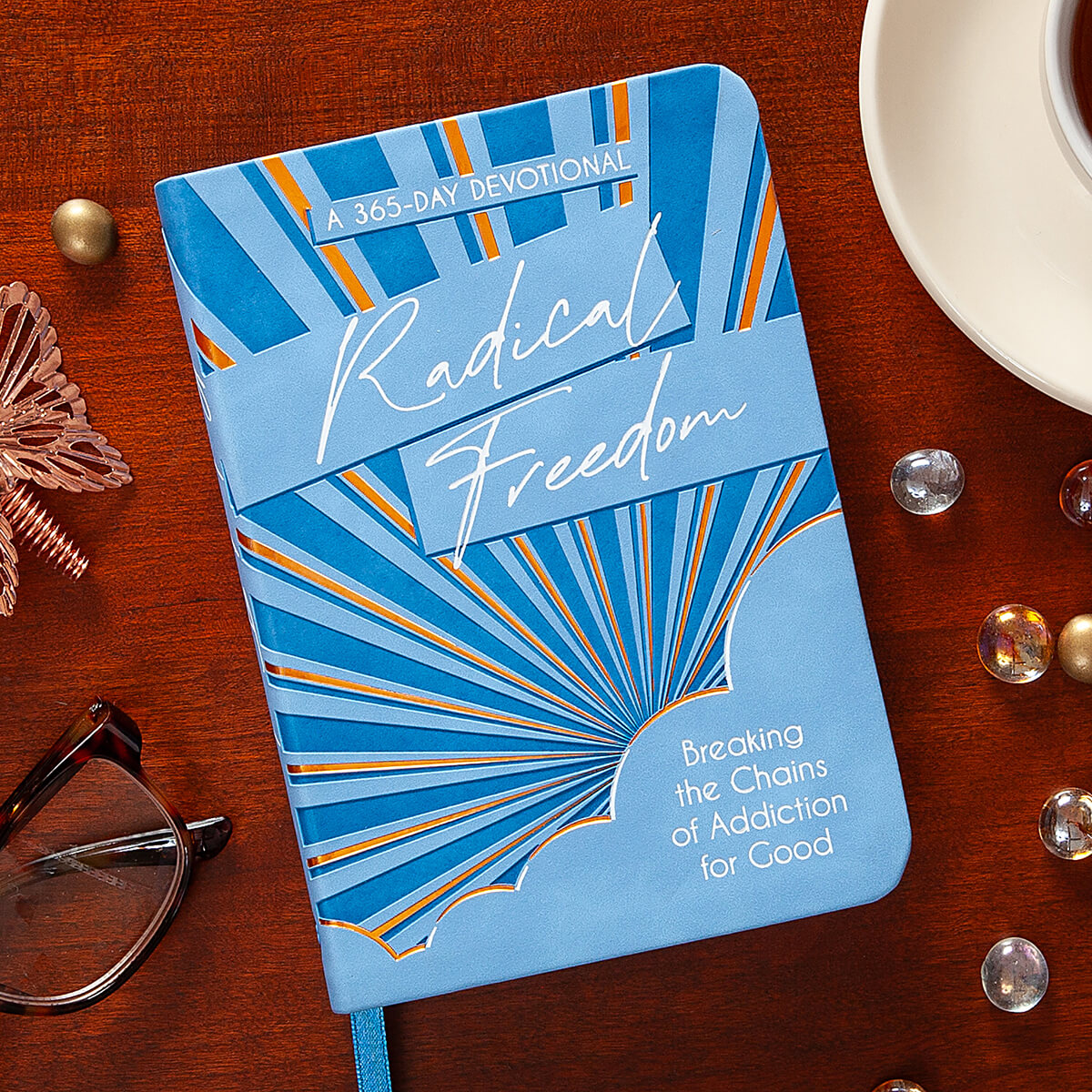 Blue devotional book titled 'Radical Freedom' on a wooden surface with glasses and a cup.