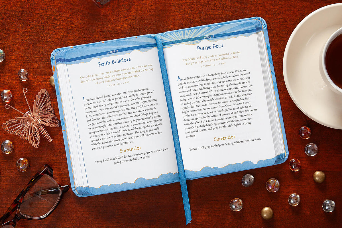 Open devotional with text on a wooden surface with a cup of tea and glasses.