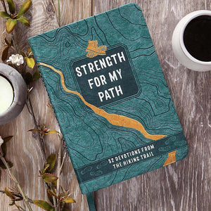 Book titled 'Strength for My Path' on a wooden surface with a cup of coffee and candle.