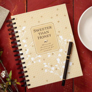 Notebook titled 'Sweeter Than Honey' on a red surface with a pen and small bowl.