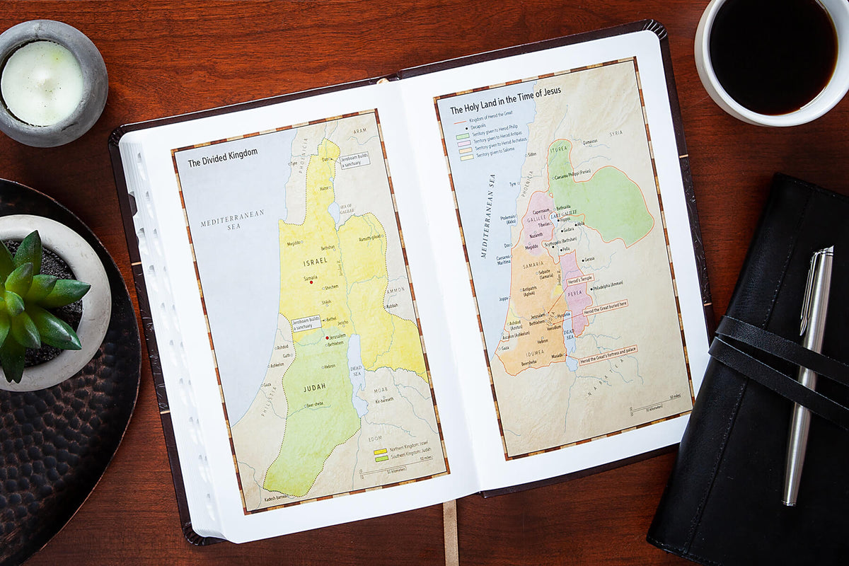 Open Bible with maps of the Holy Land on a wooden table with a cup of coffee and candle.