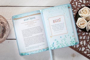 Open daily devotional with 'August' page on a wooden surface with decorative elements.
