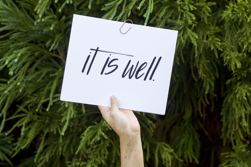 A hand holding a sign that says “It is well.”