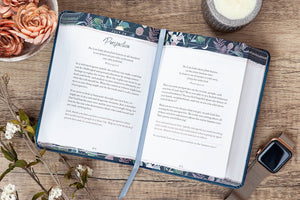 Open book on a wooden surface with floral decorations and a candle