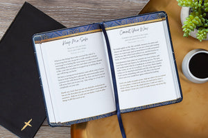 Open devotional with text on a wooden surface next to a coffee cup and plant