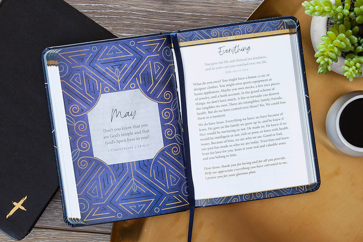 Open Biblical notebook with geometric blue design on a wooden surface with a plant and coffee cup.