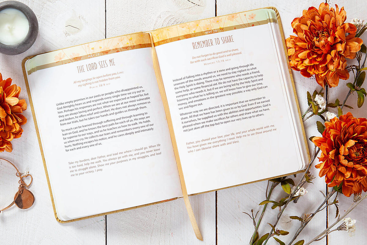 Open book with text on a wooden surface with orange flowers and a candle.