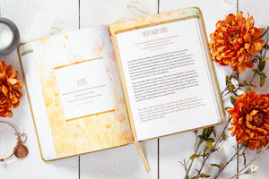Open book with decorative pages on a wooden surface with orange flowers.