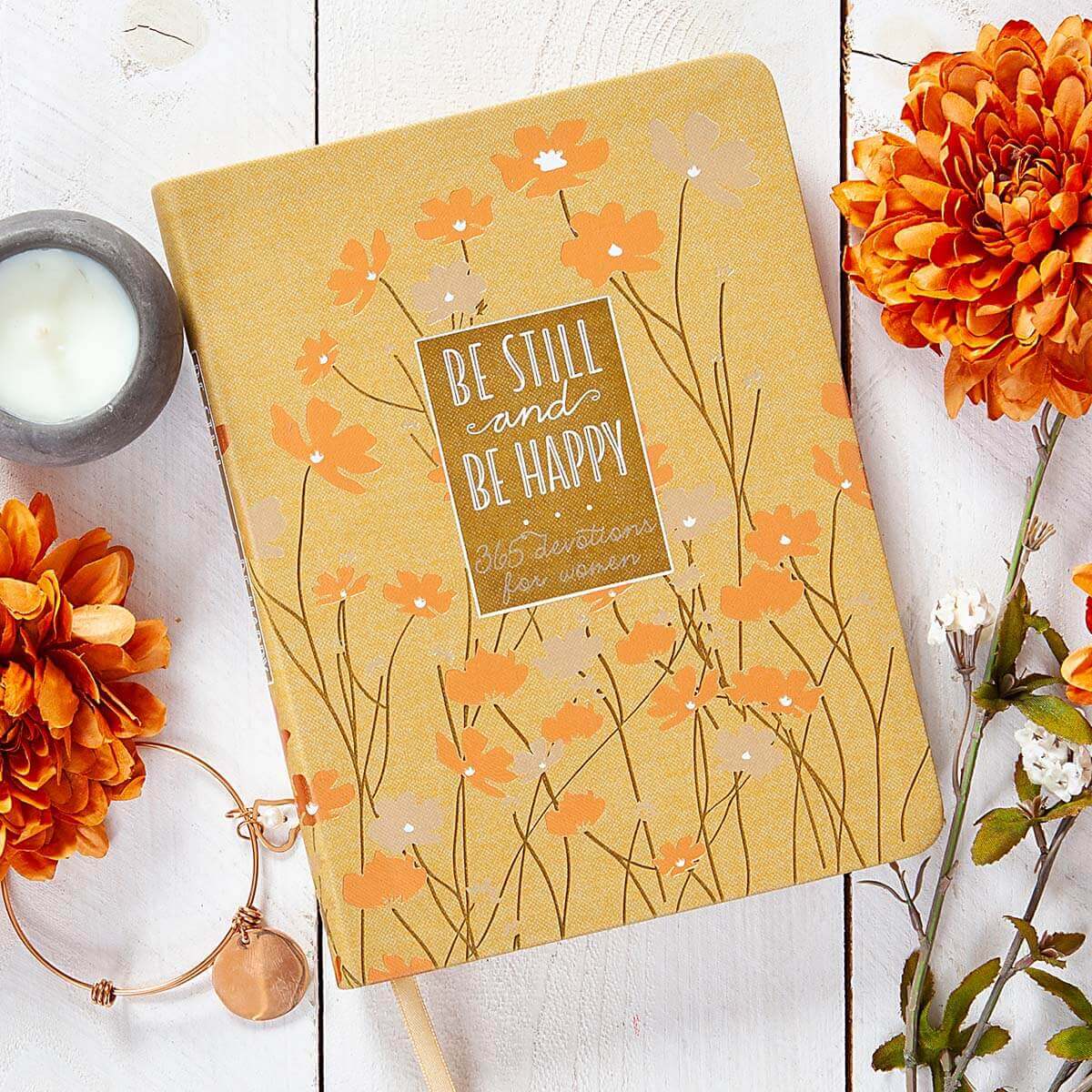 Notebook with floral design and motivational quote on a wooden surface with flowers and a candle.