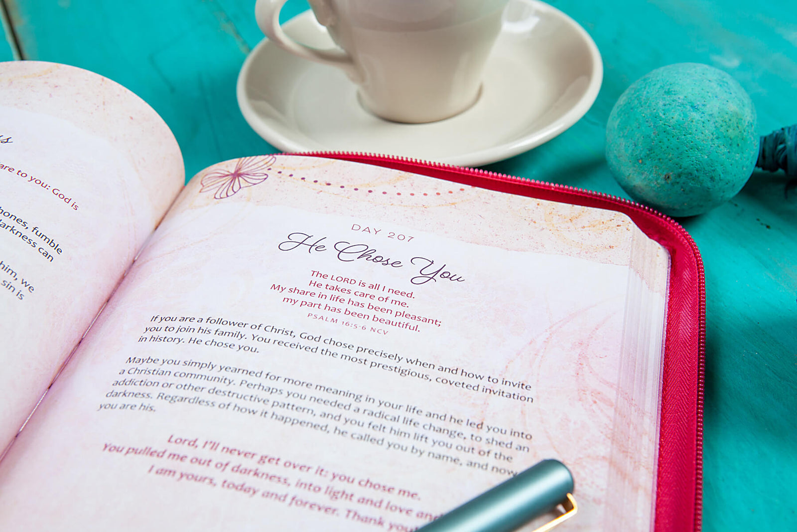 Pink devotional book with floral designs and 'Be Still and Know' text on a teal surface.
