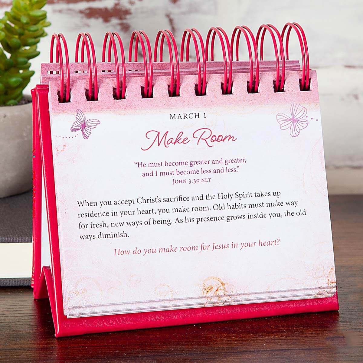 Pink devotional book titled 'Be Still and Know' with floral and butterfly designs on a wooden surface.