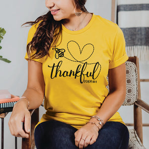 Woman sitting in a chair wearing the bee thankful Psalm 100:4 top