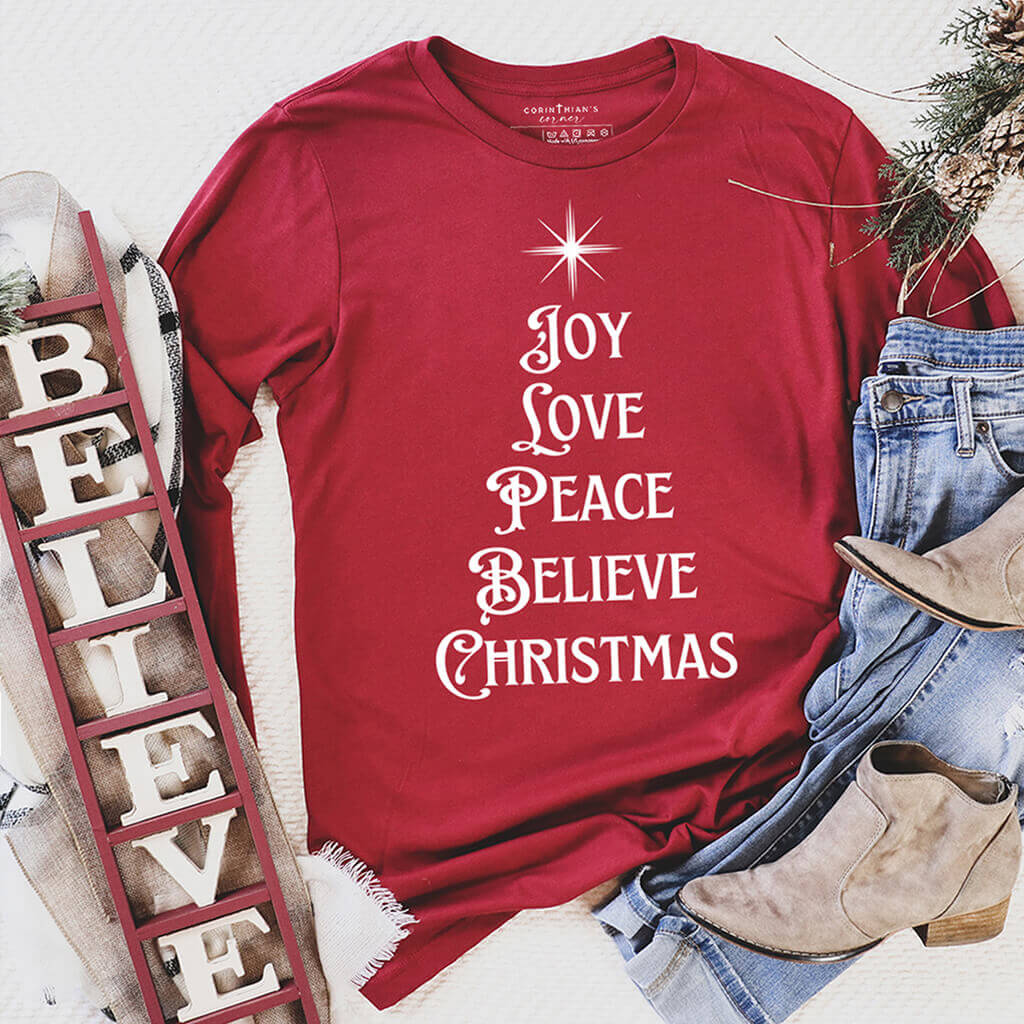 A festive 'Joy Love Peace Believe Christmas' design in white on a cardinal long sleeve