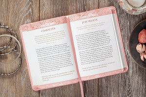 An open book with pink floral-patterned cover pages and a pink ribbon bookmark, photographed from above on a rustic wooden surface with decorative props around it.