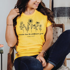 Seated woman wearing the consider how the wildflowers grow shirt