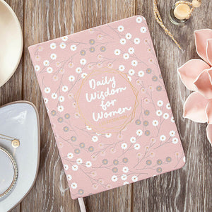 Pink notebook with floral design and 'Daily Wisdom for Women' text on a wooden surface.
