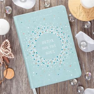 Light blue notebook with 'Detox for the Soul' text on a wooden surface with decorative items.