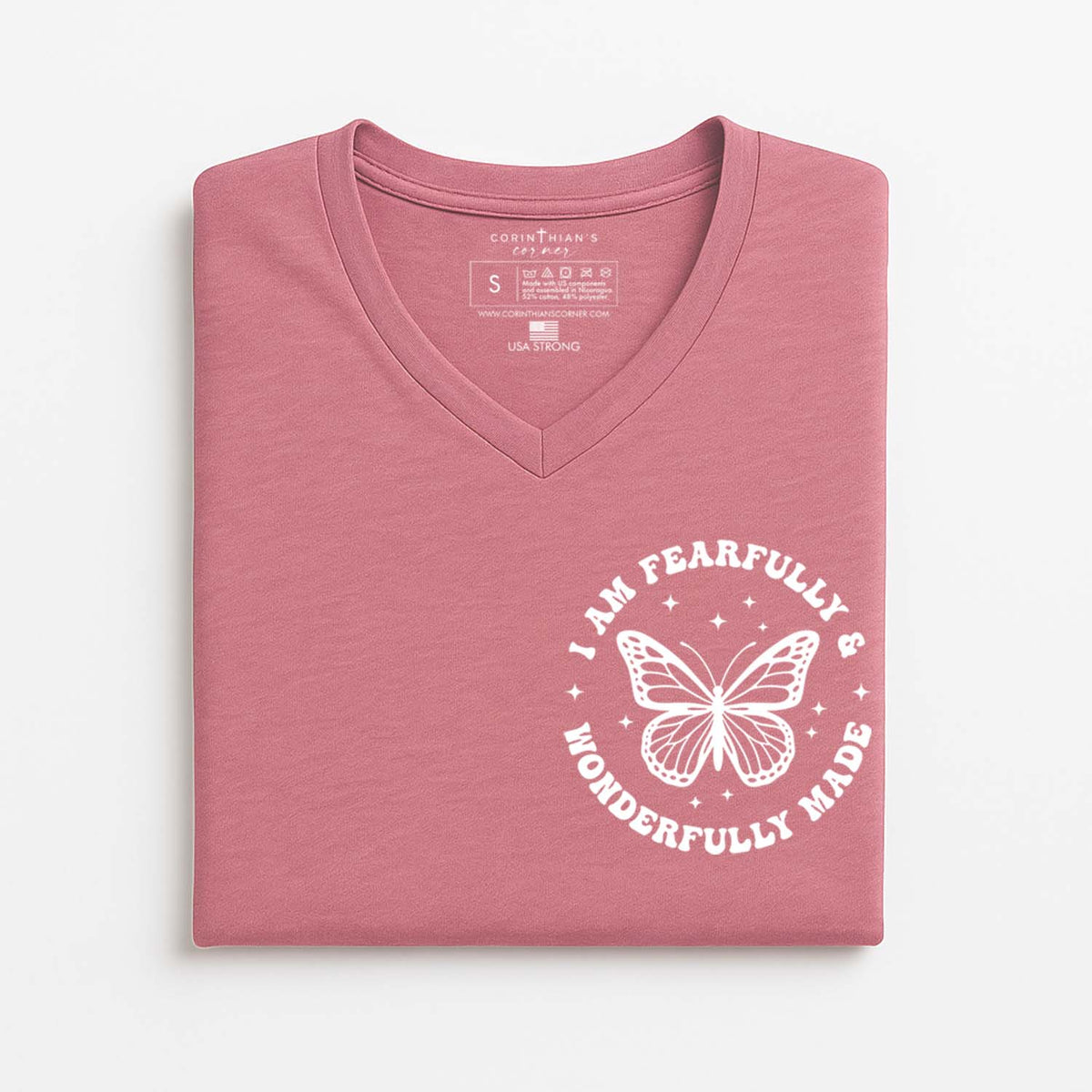 Folded pink t-shirt with a white butterfly Christian graphic on a light gray background