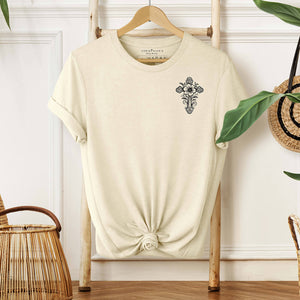 Ornate cross design on the left chest of a natural colored premium t-shirt