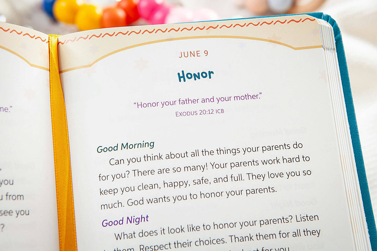 An open Bible or prayer journal showing a printed page with the heading 'HONOR' and a scripture reference, photographed close up with a colorful ribbon bookmark and blurred decorative items in the background.
