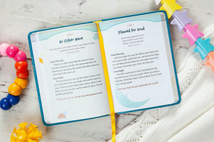 An open personalized Bible journal with a turquoise cover and a yellow ribbon bookmark, displayed on a white textured fabric with colorful star and bead props.