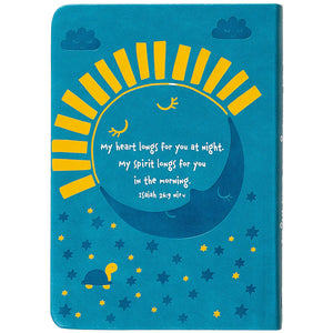 A hardcover notebook or journal with a blue cover featuring a crescent moon, yellow sun rays, stars, clouds, and a turtle, with the text 'My heart longs for you at night. My Spirit longs for you in the morning.