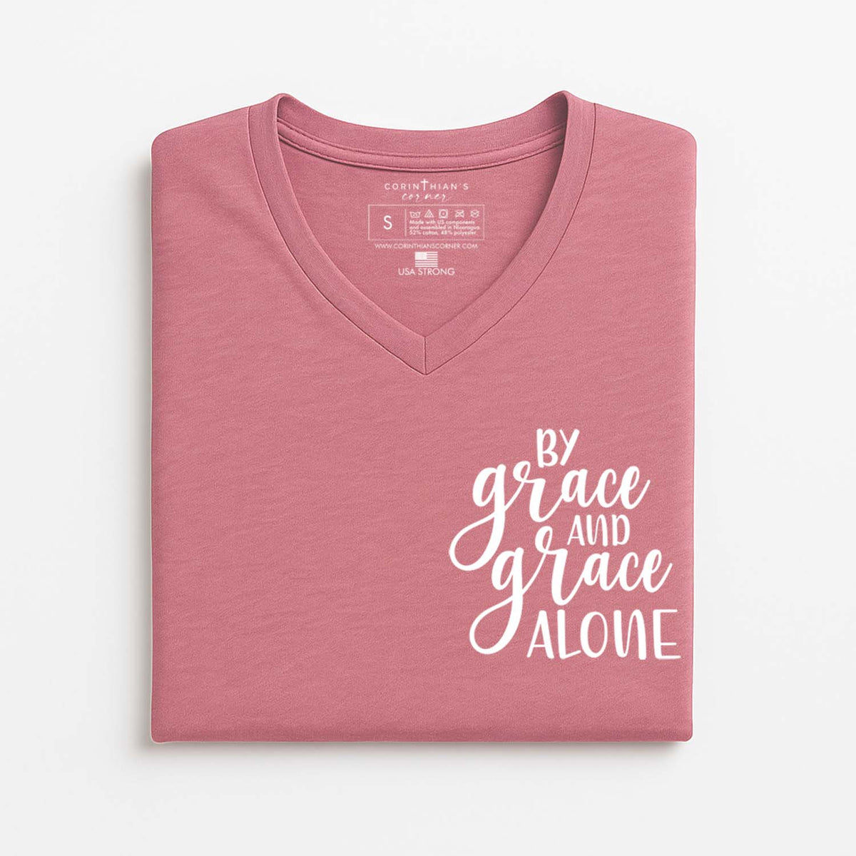 Folded pink t-shirt with 'By grace and grace alone' text on a white background