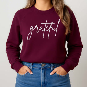 Maroon sweatshirt with 'grateful' text worn by a woman standing against a plain background
