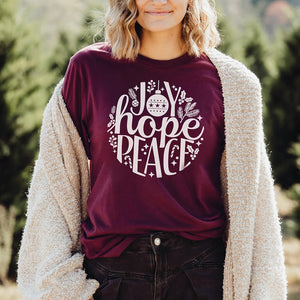 Outdoor model wearing the maroon Christmas t-shirt that reads joy hope peace