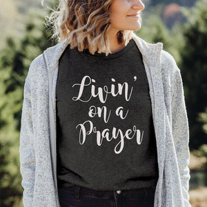 Female model wearing a grey Christian top that reads livin' on a prayer