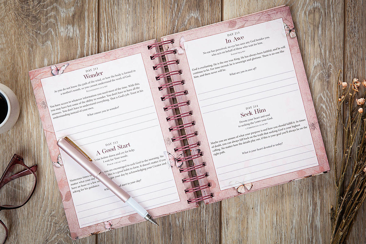 Open spiral-bound notebook with pink cover and pen on a wooden surface