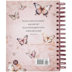 A spiral-bound notebook or journal shown from the back, featuring a pale pink background with illustrated butterflies, a Bible verse from Psalm 27:1, a barcode, and a round 'Bible Bites' logo.