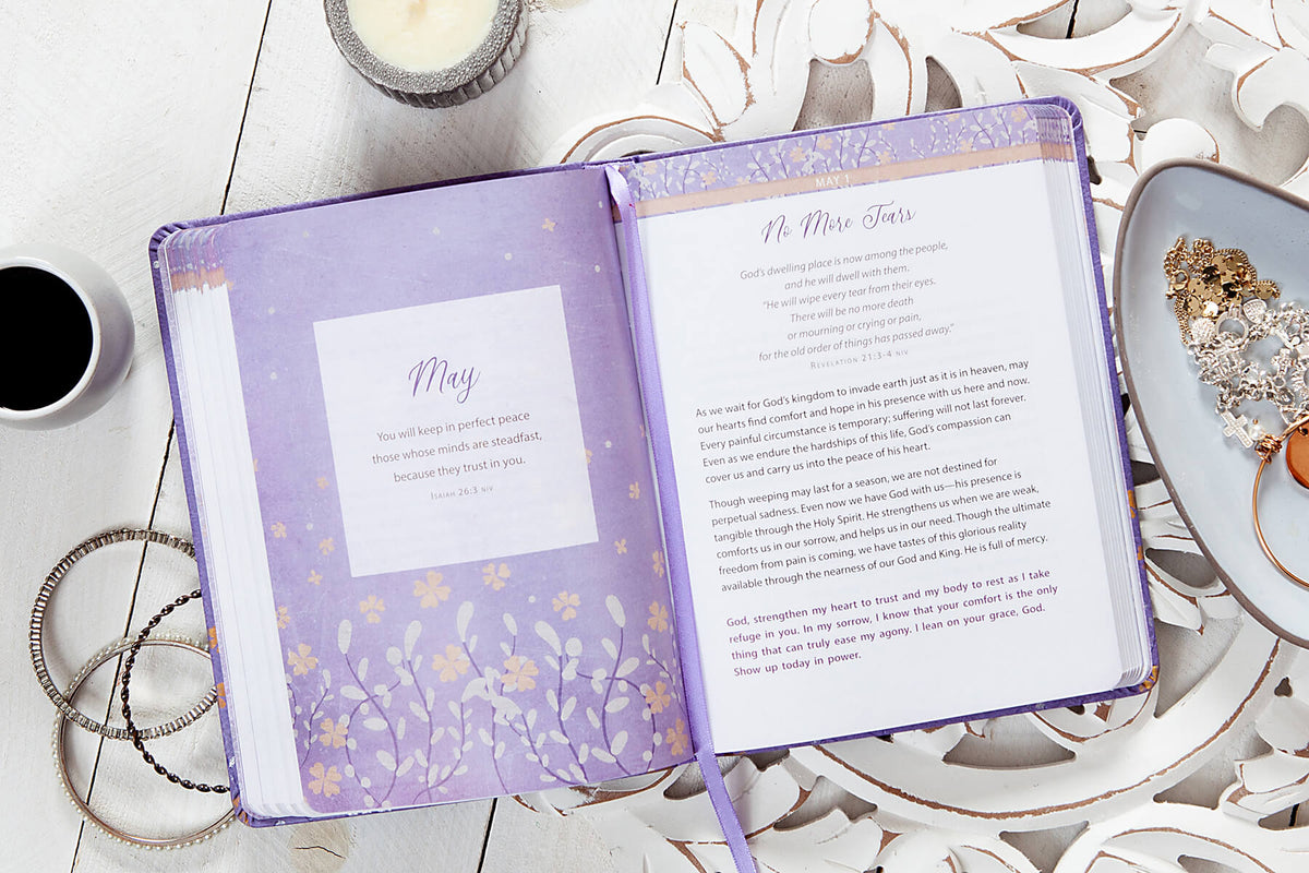 Open book with decorative purple cover on a white surface with a cup of coffee and decorative items.
